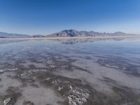 the ocean and mountains are reflected in the shallow water of the desert beach, near the horizon