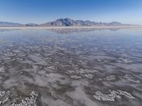 the ocean and mountains are reflected in the shallow water of the desert beach, near the horizon