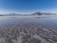 the ocean and mountains are reflected in the shallow water of the desert beach, near the horizon