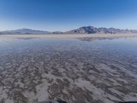 the ocean and mountains are reflected in the shallow water of the desert beach, near the horizon