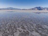 the ocean and mountains are reflected in the shallow water of the desert beach, near the horizon