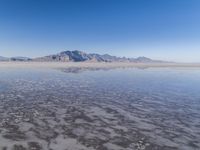 the ocean and mountains are reflected in the shallow water of the desert beach, near the horizon