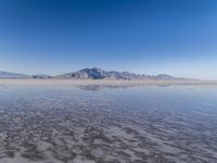 the ocean and mountains are reflected in the shallow water of the desert beach, near the horizon