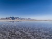 the ocean and mountains are reflected in the shallow water of the desert beach, near the horizon