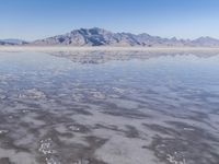 the ocean and mountains are reflected in the shallow water of the desert beach, near the horizon