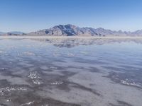 the ocean and mountains are reflected in the shallow water of the desert beach, near the horizon