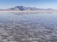 the ocean and mountains are reflected in the shallow water of the desert beach, near the horizon