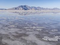 the ocean and mountains are reflected in the shallow water of the desert beach, near the horizon