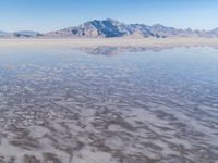 the ocean and mountains are reflected in the shallow water of the desert beach, near the horizon