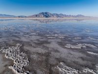 the ocean and mountains are reflected in the shallow water of the desert beach, near the horizon