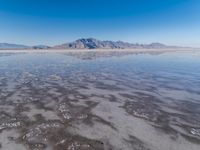 the ocean and mountains are reflected in the shallow water of the desert beach, near the horizon