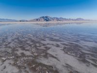 the ocean and mountains are reflected in the shallow water of the desert beach, near the horizon