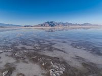 the ocean and mountains are reflected in the shallow water of the desert beach, near the horizon