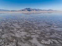 the ocean and mountains are reflected in the shallow water of the desert beach, near the horizon