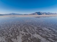 the ocean and mountains are reflected in the shallow water of the desert beach, near the horizon