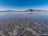 the ocean and mountains are reflected in the shallow water of the desert beach, near the horizon