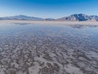 the ocean and mountains are reflected in the shallow water of the desert beach, near the horizon