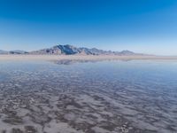 the ocean and mountains are reflected in the shallow water of the desert beach, near the horizon