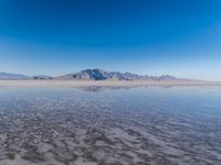 the ocean and mountains are reflected in the shallow water of the desert beach, near the horizon