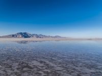 the ocean and mountains are reflected in the shallow water of the desert beach, near the horizon