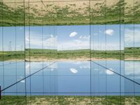 the reflection of a sky in a glass enclosure reflecting the green hills and blue skies