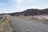 the road is going to an empty rocky area and has many rocks all around it