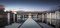 a building that is designed with glass doors and lights on and reflecting water in the pool