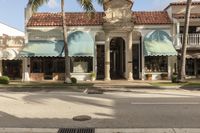 a street intersection with store fronts and palm trees, which is closed to the public