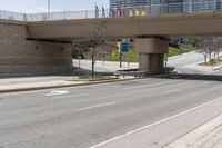 an empty highway with buildings and an overpass above it at the base of a bridge