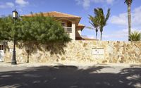 a tan stone fence with palm trees in front of it and a large house on one side