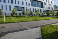 a city street surrounded by grass and tall buildings at the end of a street there is a paved pathway in front of the building