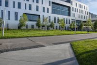 a city street surrounded by grass and tall buildings at the end of a street there is a paved pathway in front of the building