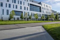 a city street surrounded by grass and tall buildings at the end of a street there is a paved pathway in front of the building