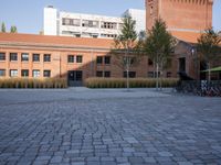 an empty square with buildings and bikes in the background behind it and trees outside on either side of the building