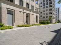 this sidewalk has multiple pavings near two buildings on the sides of it and shrubs beside the curb