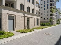 this sidewalk has multiple pavings near two buildings on the sides of it and shrubs beside the curb