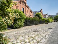 an alley with cobblestone roads and a building that is red brick and surrounded by trees