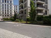 empty paved city street with two buildings in background, with cobblestone pavement and steps on sidewalk