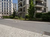 empty paved city street with two buildings in background, with cobblestone pavement and steps on sidewalk