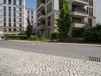 empty paved city street with two buildings in background, with cobblestone pavement and steps on sidewalk