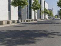 an empty sidewalk with a few trees on either side and one parked vehicle on the other