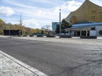 a view of a street in front of a building, with benches and buildings around the perimeter