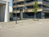 a building with a couple of people riding bikes on the sidewalk below it with cobbles on a paved road