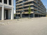 a building with a couple of people riding bikes on the sidewalk below it with cobbles on a paved road