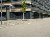 a building with a couple of people riding bikes on the sidewalk below it with cobbles on a paved road