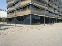 a building with a couple of people riding bikes on the sidewalk below it with cobbles on a paved road