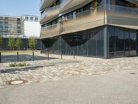 a building with a couple of people riding bikes on the sidewalk below it with cobbles on a paved road