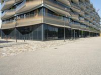 a building with a couple of people riding bikes on the sidewalk below it with cobbles on a paved road