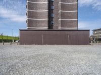 a building with a tower made of bricks is next to a park benches on gravel