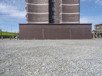 a building with a tower made of bricks is next to a park benches on gravel